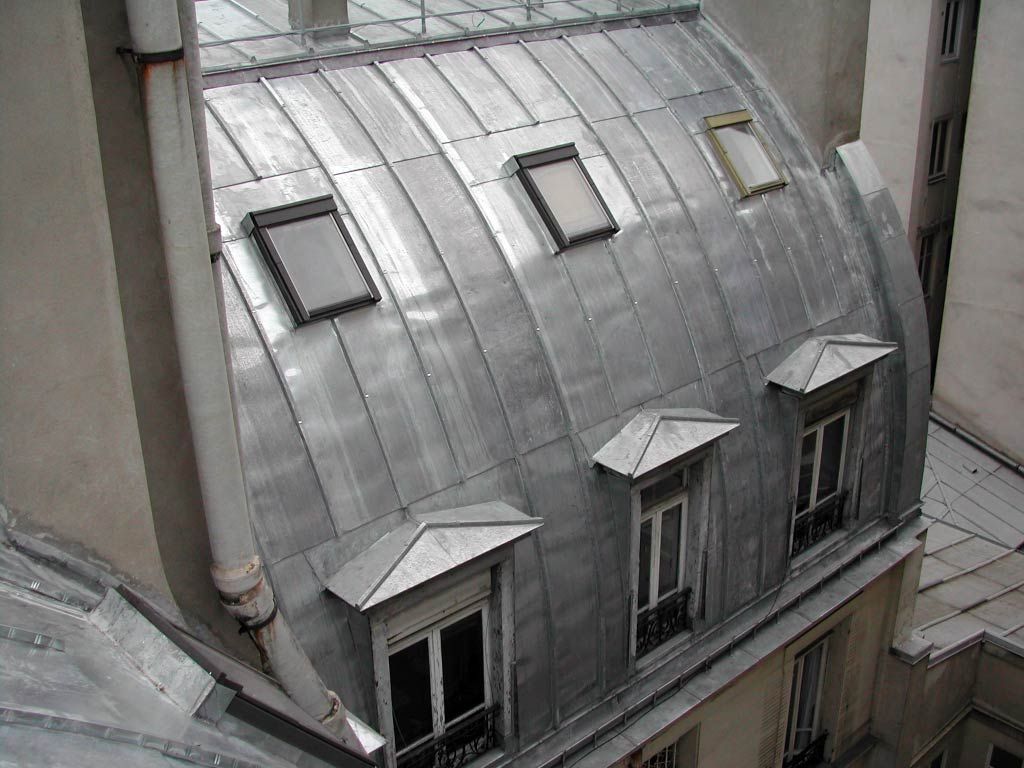 Toiture argentée incurvée avec lucarnes et puits de lumière entre les murs du bâtiment