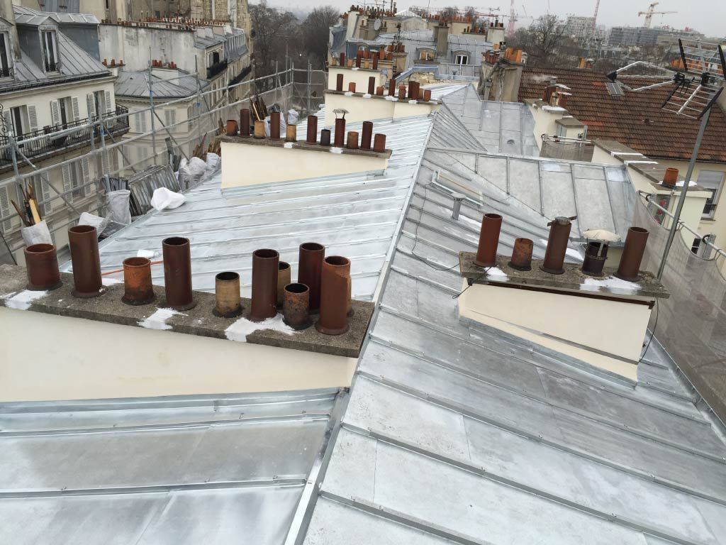 Toits aux surfaces goudronnées blanches et aux nombreuses cheminées en briques dans un quartier urbain sous un ciel couvert