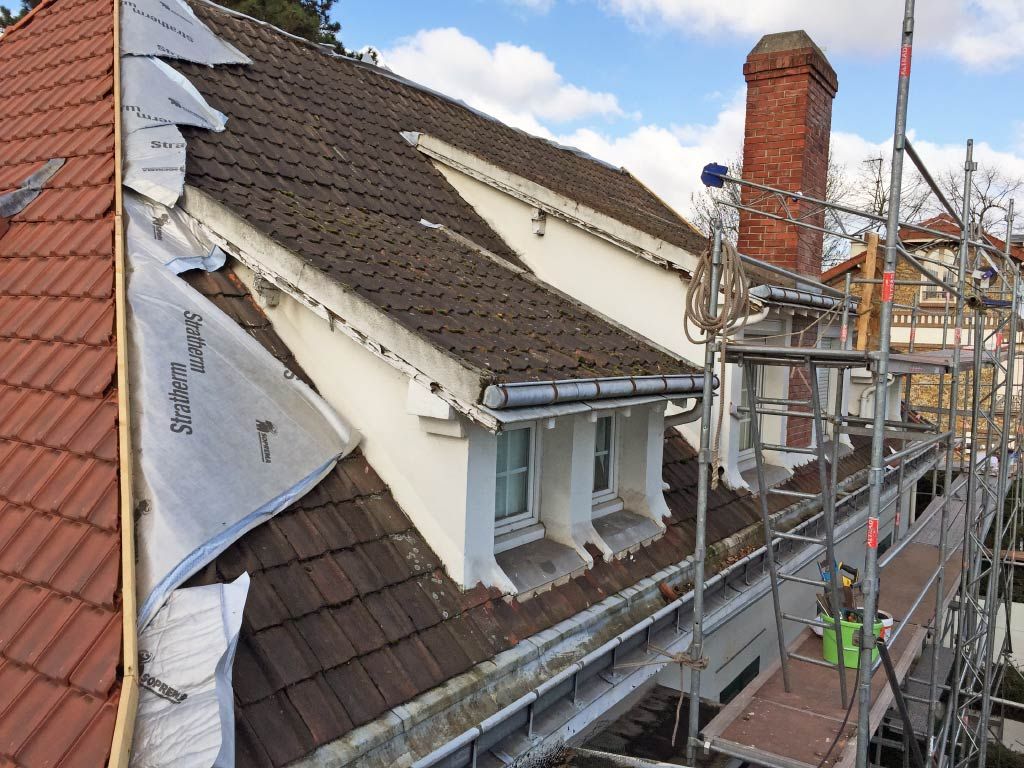 Toiture en construction avec échafaudages, cheminée et bâches de protection sur une maison