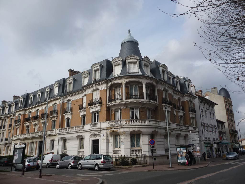 Angle d'un immeuble parisien historique à toit mansardé et voitures garées dans une rue nuageuse