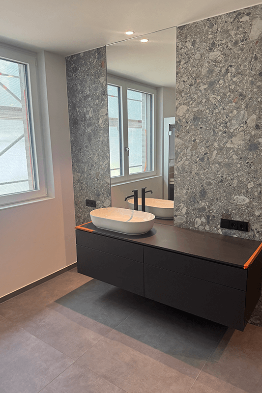 Modernes Badezimmer mit schwebendem grauen Schrank, Aufsatzwaschbecken und großem Spiegel vor strukturierter Wand.