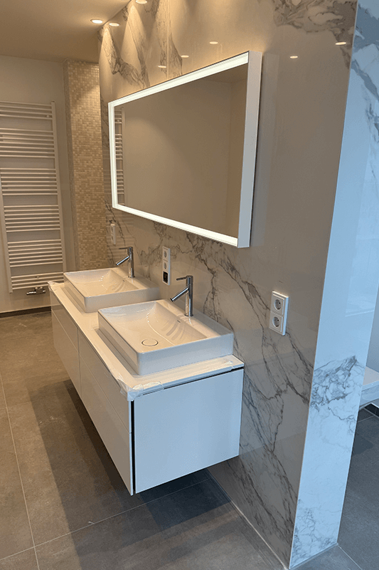 Modernes weißes Badezimmer mit Doppelwaschbecken, großem Spiegel und Marmorwandfliesen.