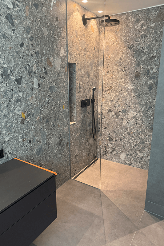 Moderne Dusche mit grauen Fliesen im Terrazzo-Stil, Glastür und schwarzen Armaturen.