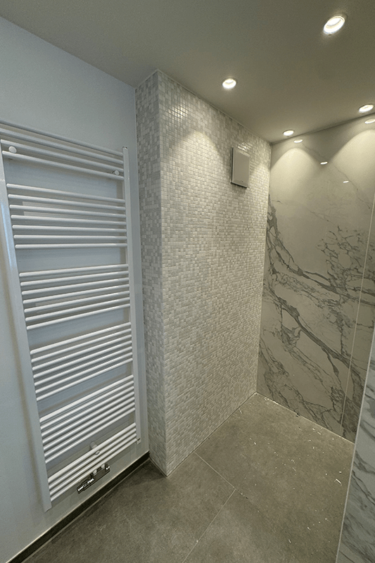 Modernes Badezimmer mit weißem Heizkörper, grau gefliesten Wänden und Einbauleuchten.