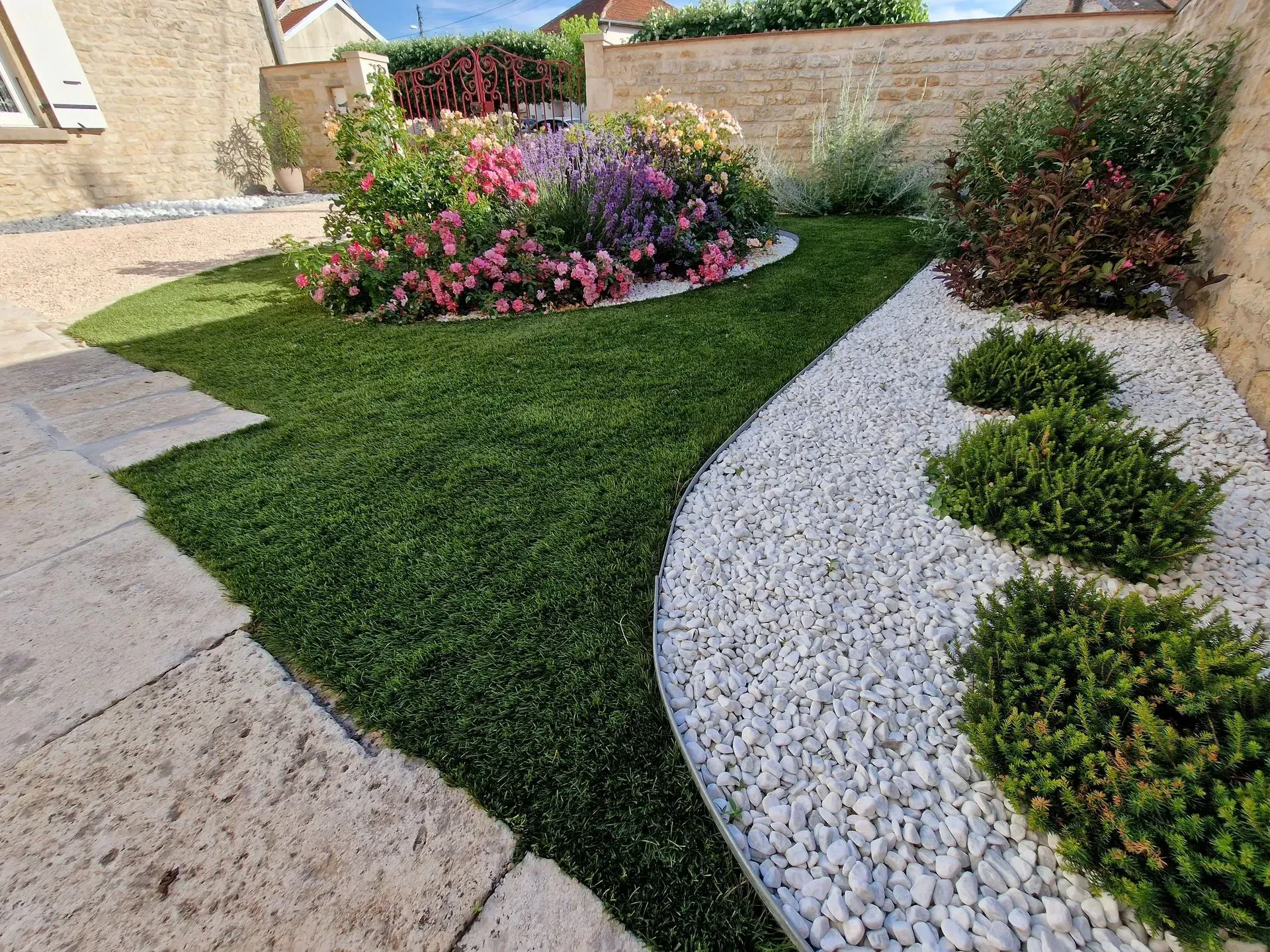 Une pelouse impeccable bordée de pierres blanches, un parterre de fleurs éclatant et une allée de pierres dans un jardin paysager ensoleillé.