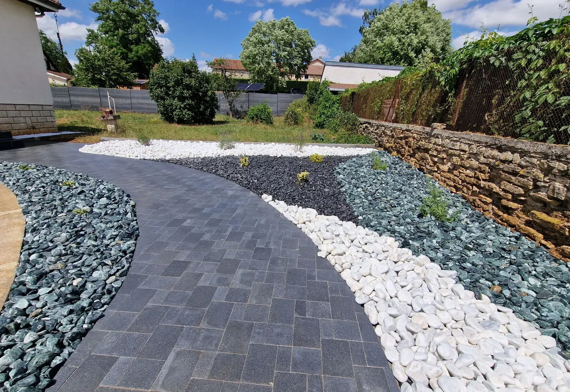 Une allée pavée serpente à travers un jardin paysager orné de motifs de pierres décoratives blanches, noires et grises.