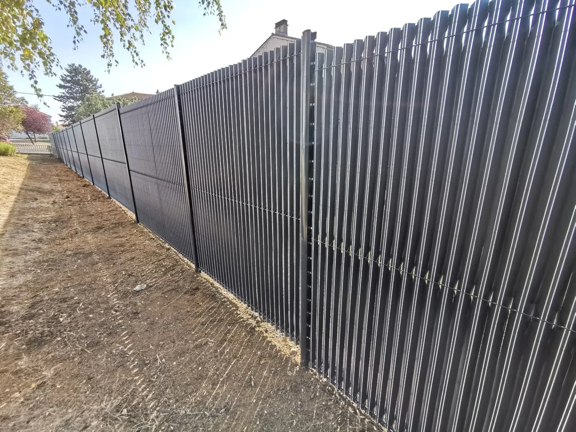 Une longue clôture souple de couleur grise le long d'un terrain ensoleillé.