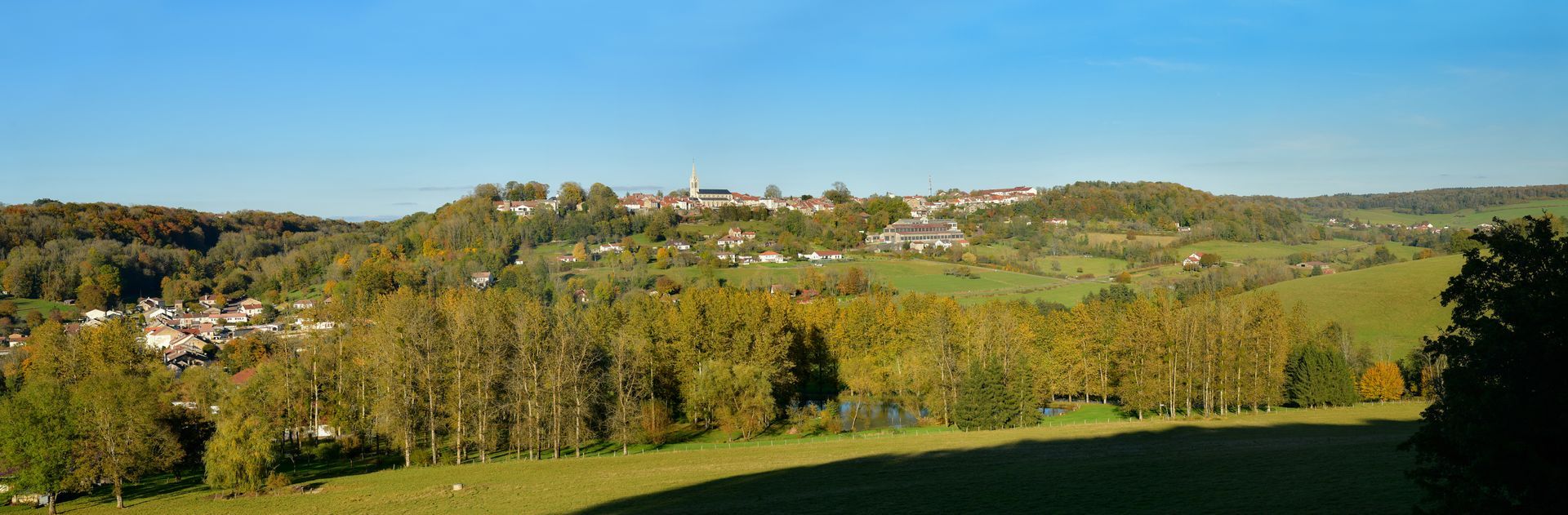 Vue panoramique de la ville de Nogent nichée sur une colline verdoyante et vallonnée, sous un ciel bleu azur par une belle journée.