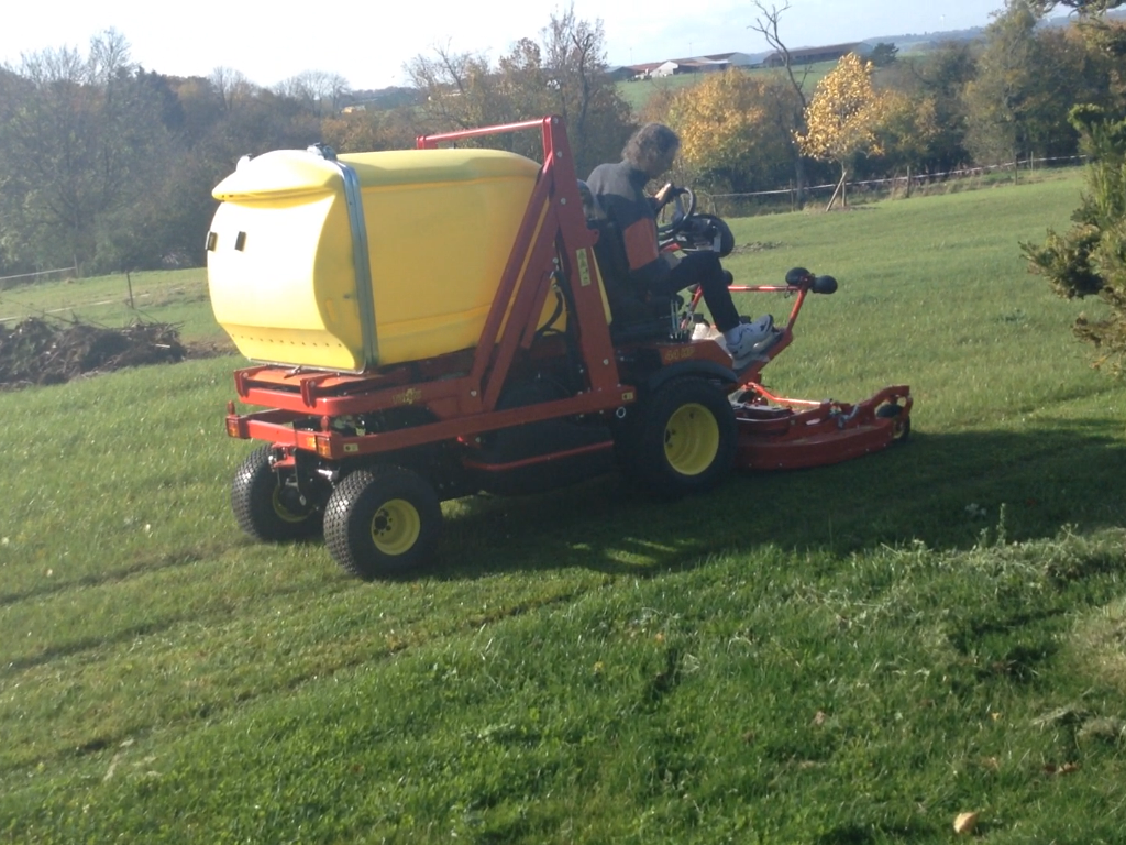 Une personne conduit une tondeuse autoportée avec un grand réservoir de dans un parc.