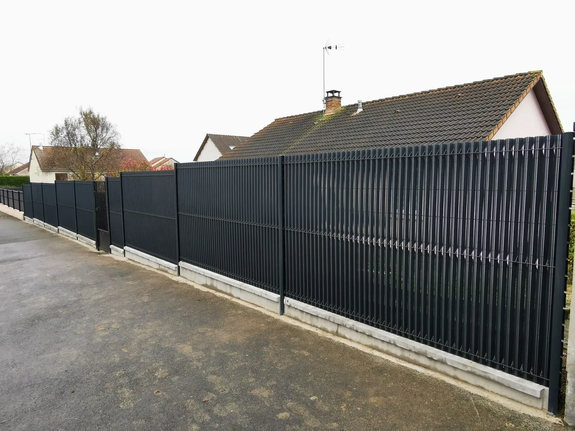 Clôture d'intimité noire à lattes verticales et sections en treillis.