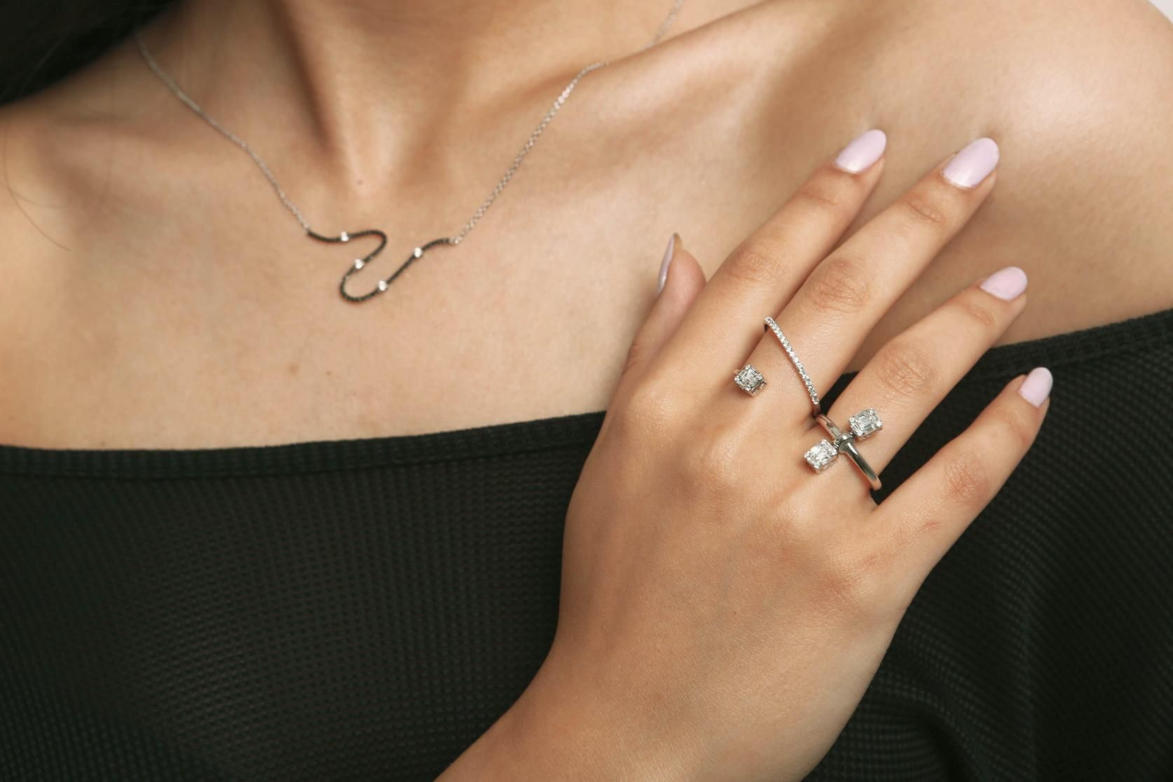 Mano con anillos y collar de plata sobre una blusa negra