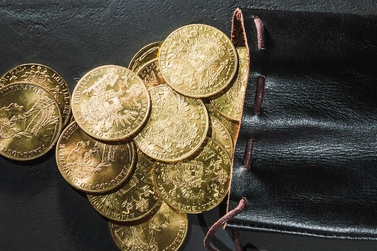Montón de monedas de color dorado sobre tela oscura, con algunas apiladas a lo largo del borde derecho.