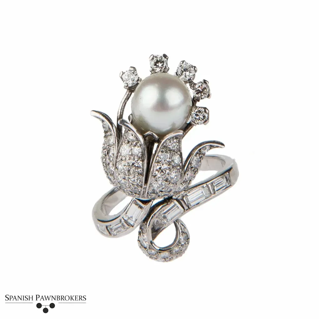Broche floral de perlas y diamantes con detalles de cinta plateada sobre fondo blanco.