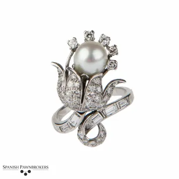Broche floral de perlas y diamantes con detalles de cinta plateada sobre fondo blanco.