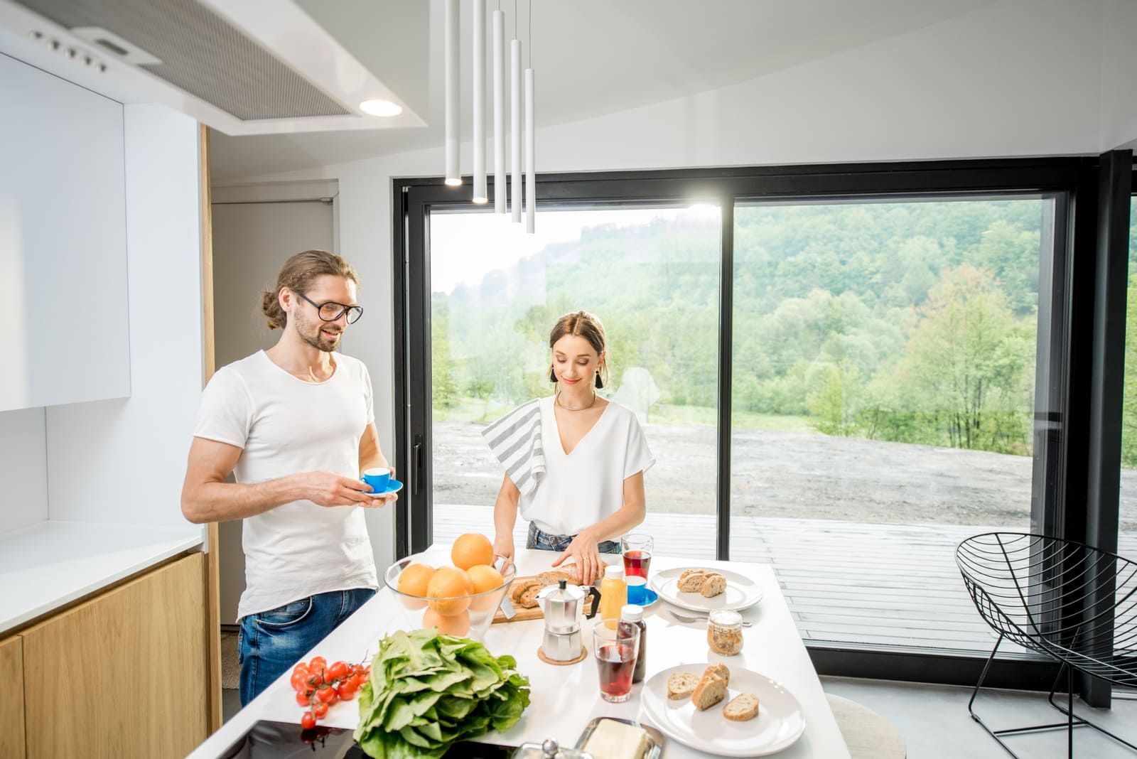 Deux personnes dans une cuisine avec de nombreux aliments devant une baie vitrée