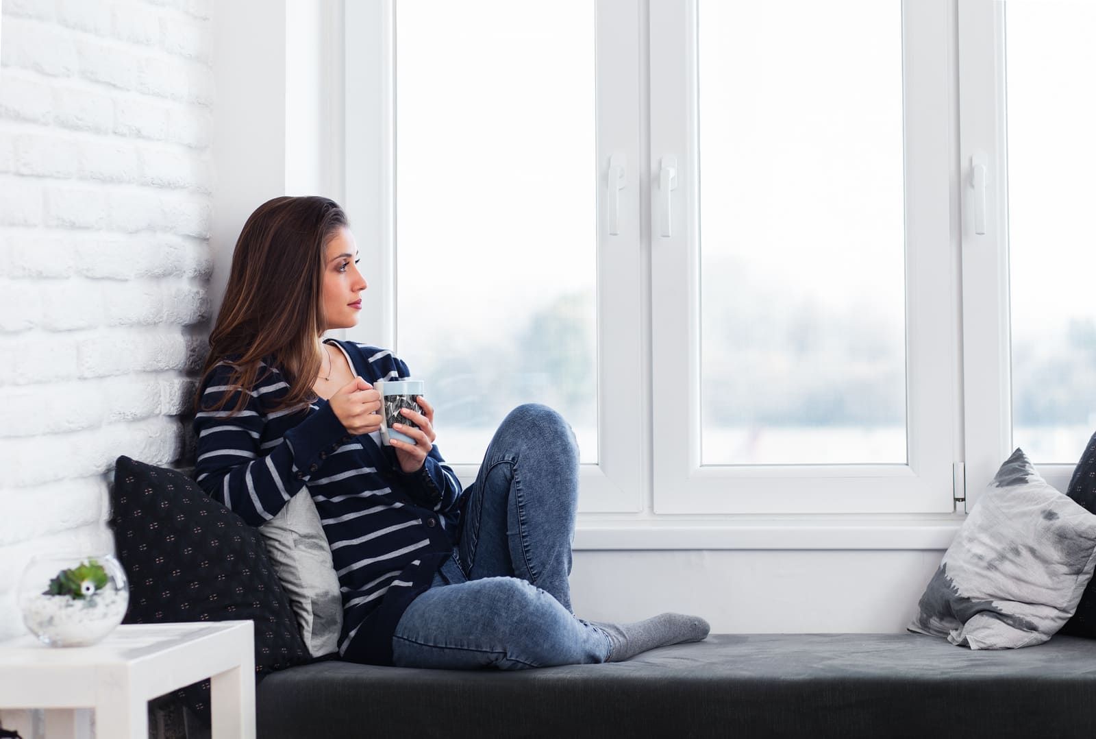 Une femme assise devant une fenêtre qui boit un café