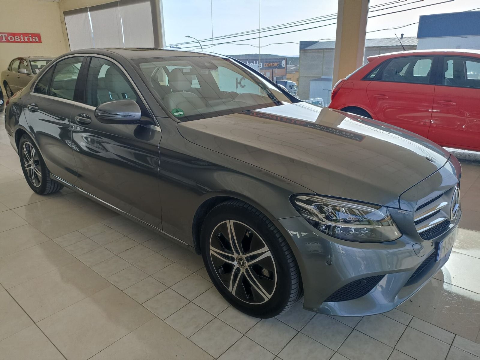 Un sedán Mercedes gris estacionado en el interior de una sala de exposición con suelo de baldosas