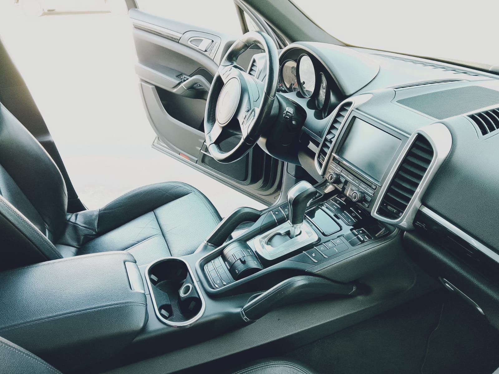Interior del coche con asientos, volante, salpicadero y consola central de cuero negro a la luz del día.