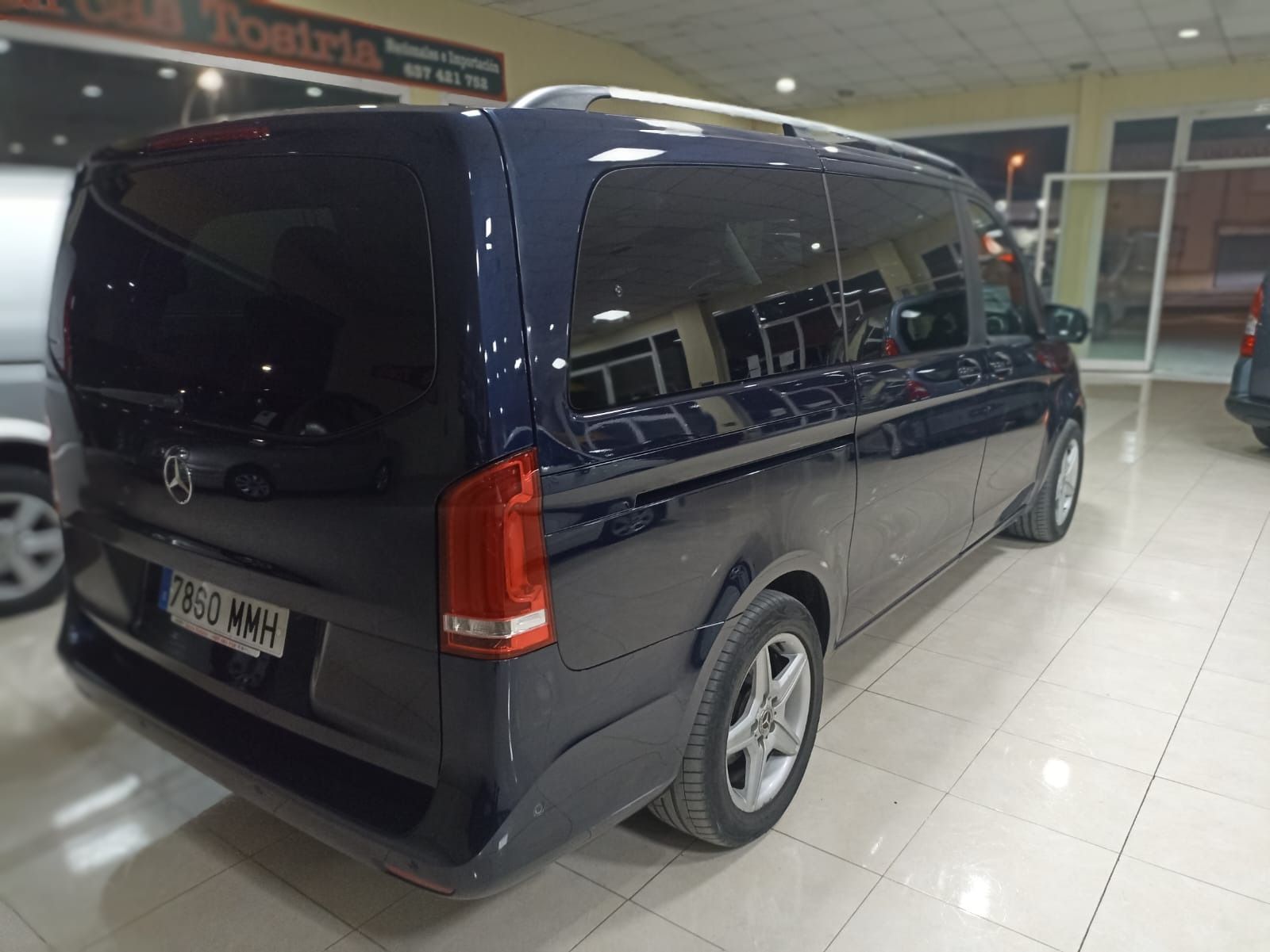 Minivan azul oscuro exhibida en una sala de exposición bien iluminada, vista trasera de tres cuartos.