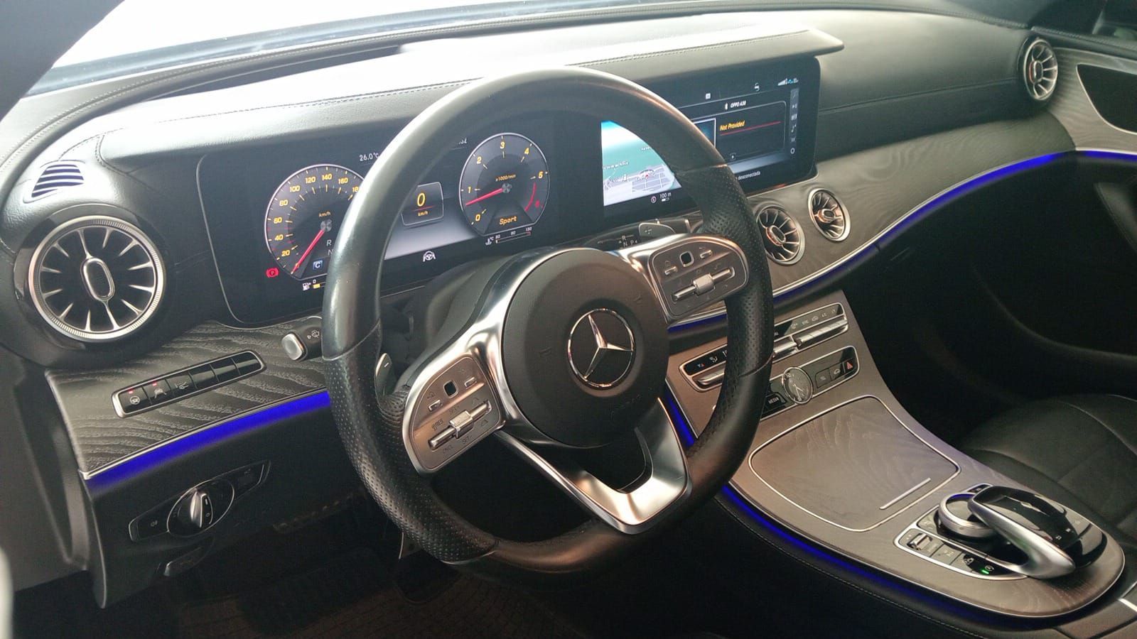 Interior de Mercedes-Benz con salpicadero iluminado, volante e iluminación ambiental azul en toda la consola.