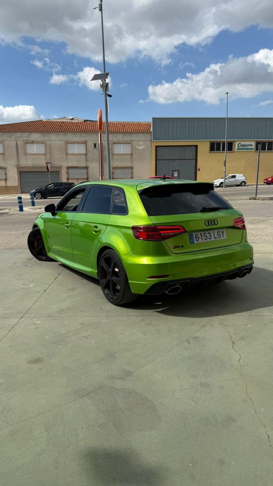 Un hatchback de color verde lima brillante estacionado en un aparcamiento al aire libre cerca de edificios industriales 