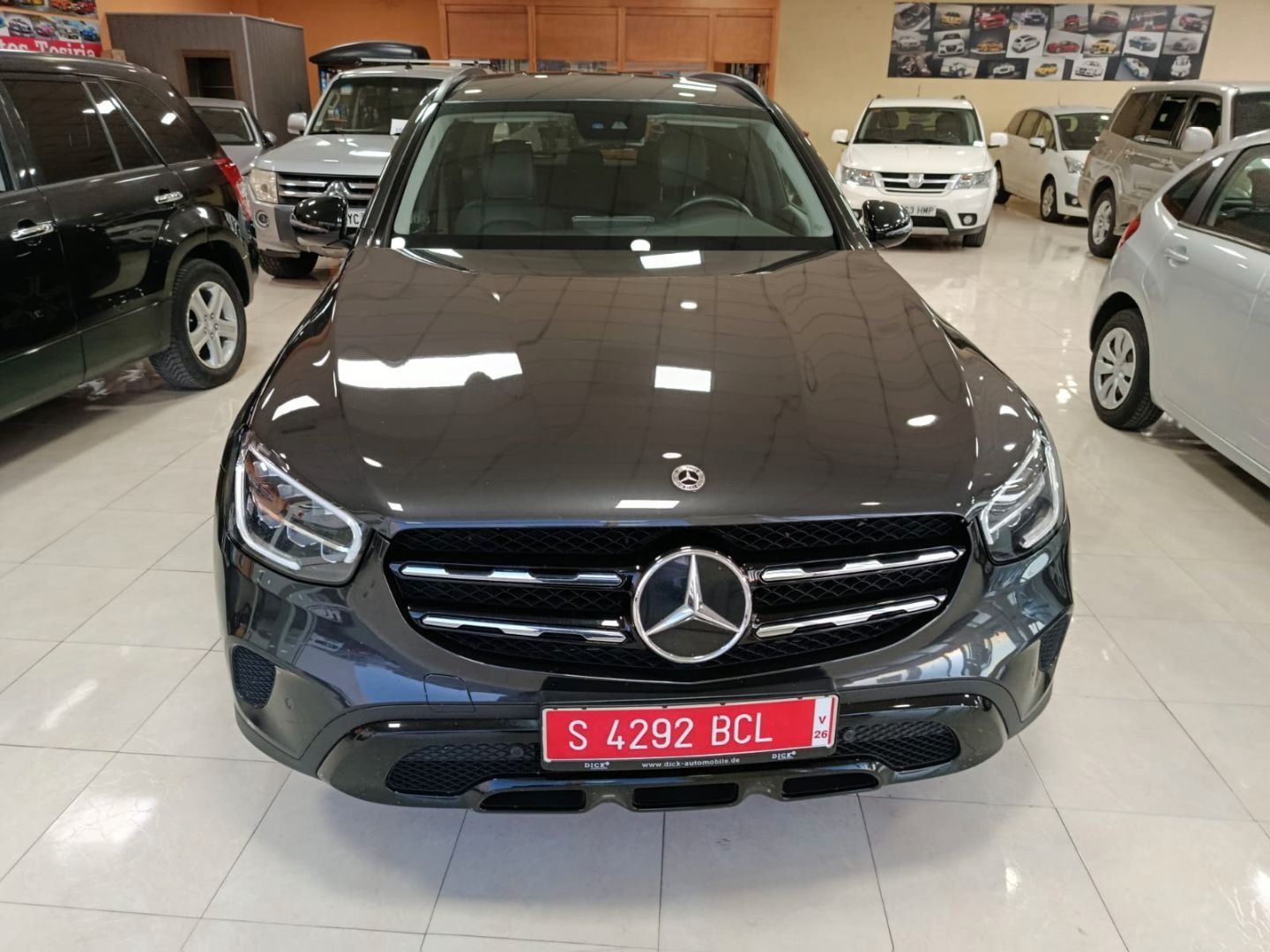 Vista frontal de un SUV Mercedes gris oscuro en una sala de exposición, con una matrícula roja.