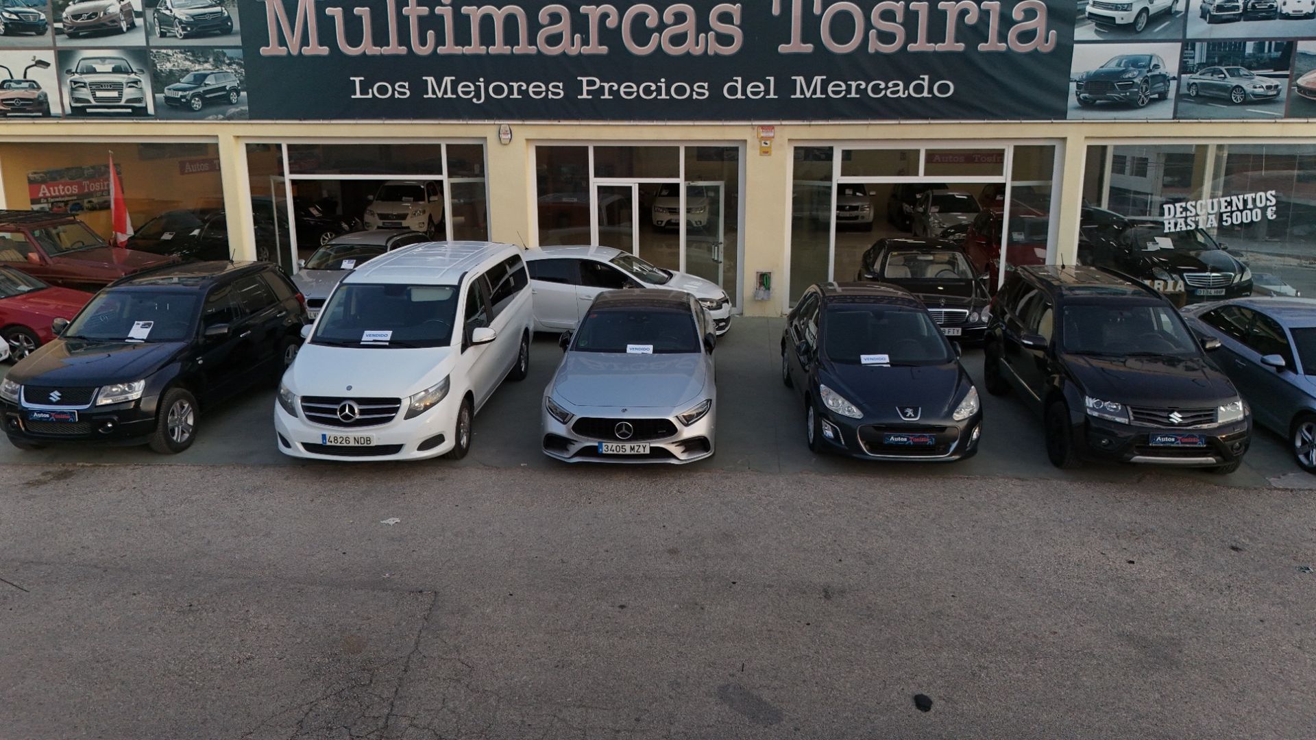 Fachada de un concesionario de coches con cinco coches aparcados en fila en el exterior
