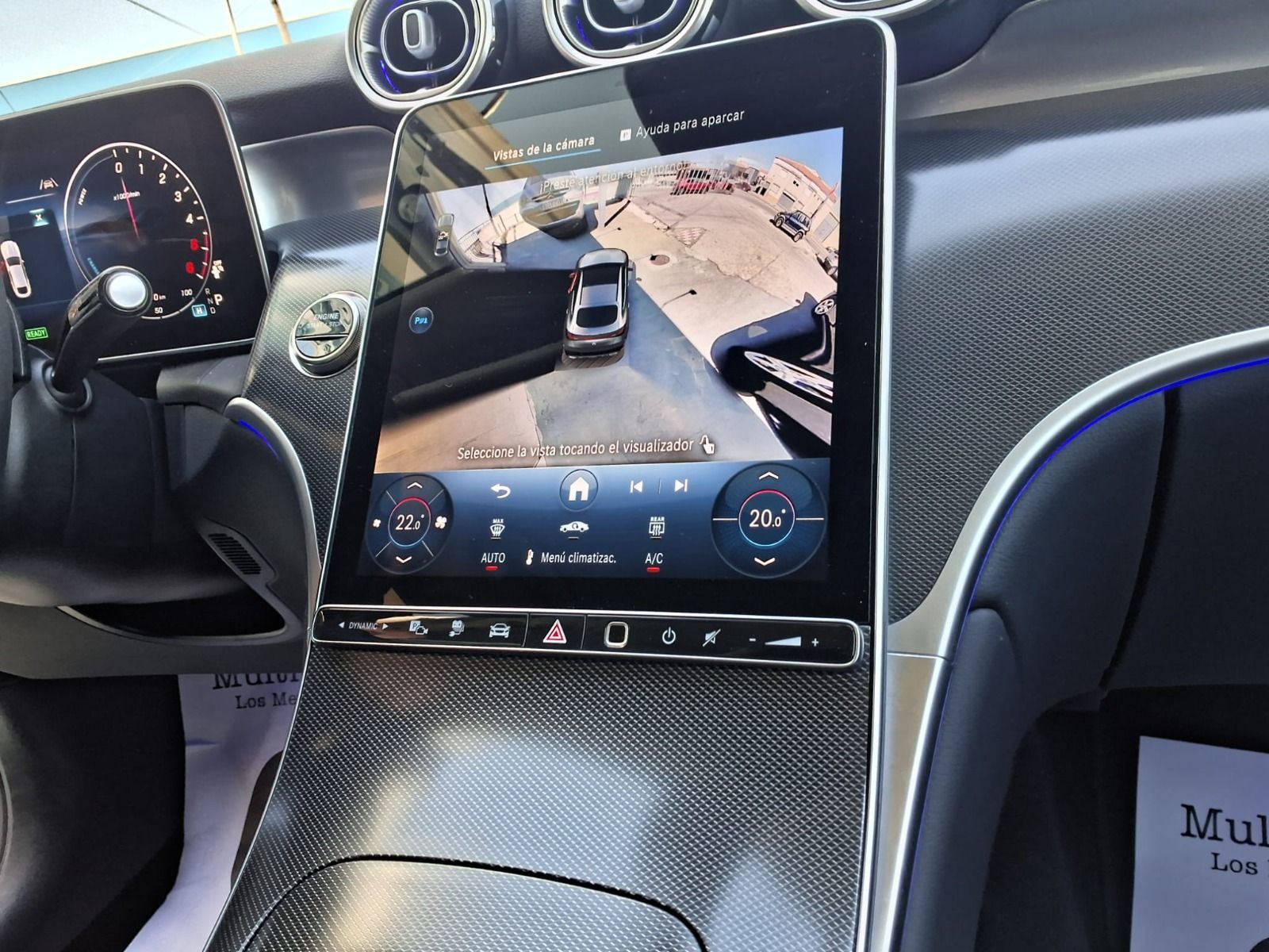 Interior de un Tesla con pantalla táctil central que muestra una cámara de visión trasera y detalles en fibra de carbono.