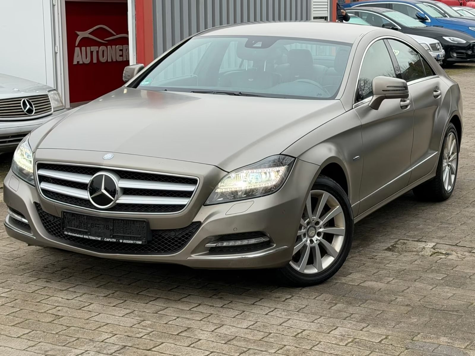 Un sedán Mercedes-Benz plateado estacionado frente a un concesionario.