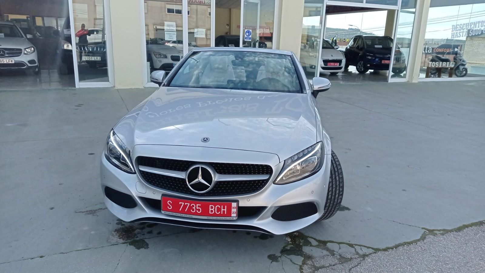 Un sedán Mercedes plateado estacionado frente a un concesionario.