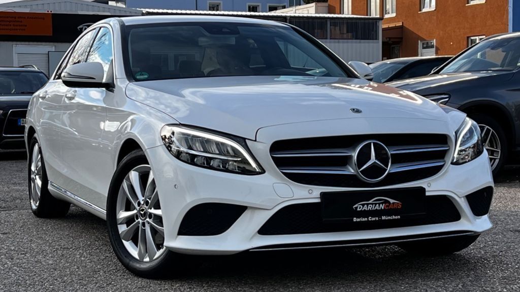 Un sedán Mercedes-Benz blanco estacionado al aire libre frente a un edificio.