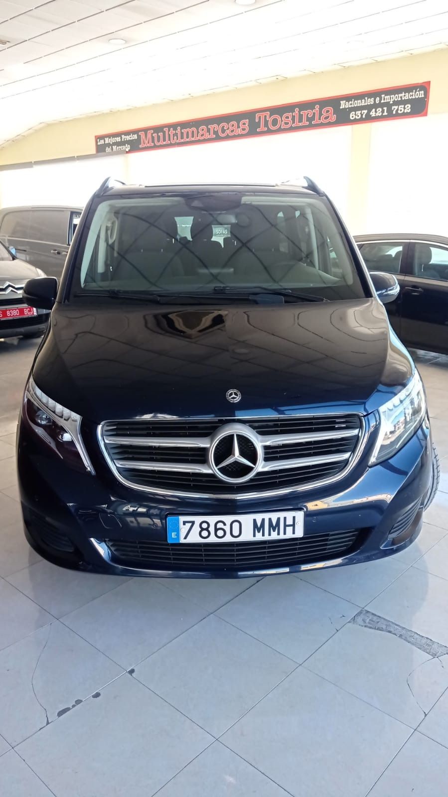 Vista frontal de una furgoneta Mercedes azul oscuro en una sala de exposición con suelo de baldosas.