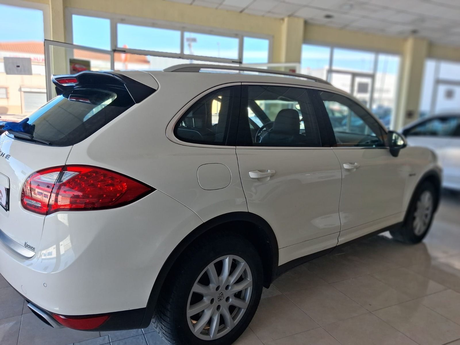 SUV blanco estacionado en el interior de una sala de exposición de automóviles, visto desde la parte trasera.