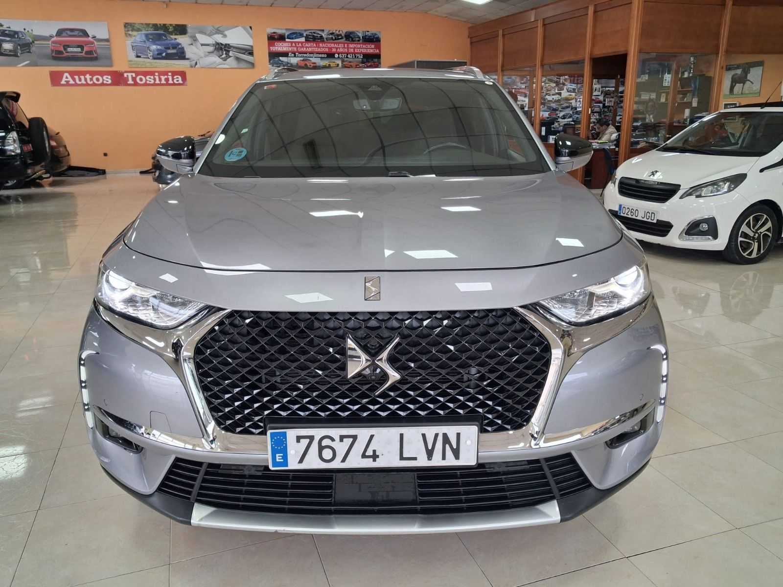 Vista frontal de un SUV DS plateado en una sala de exposición, con otros coches visibles al fondo.