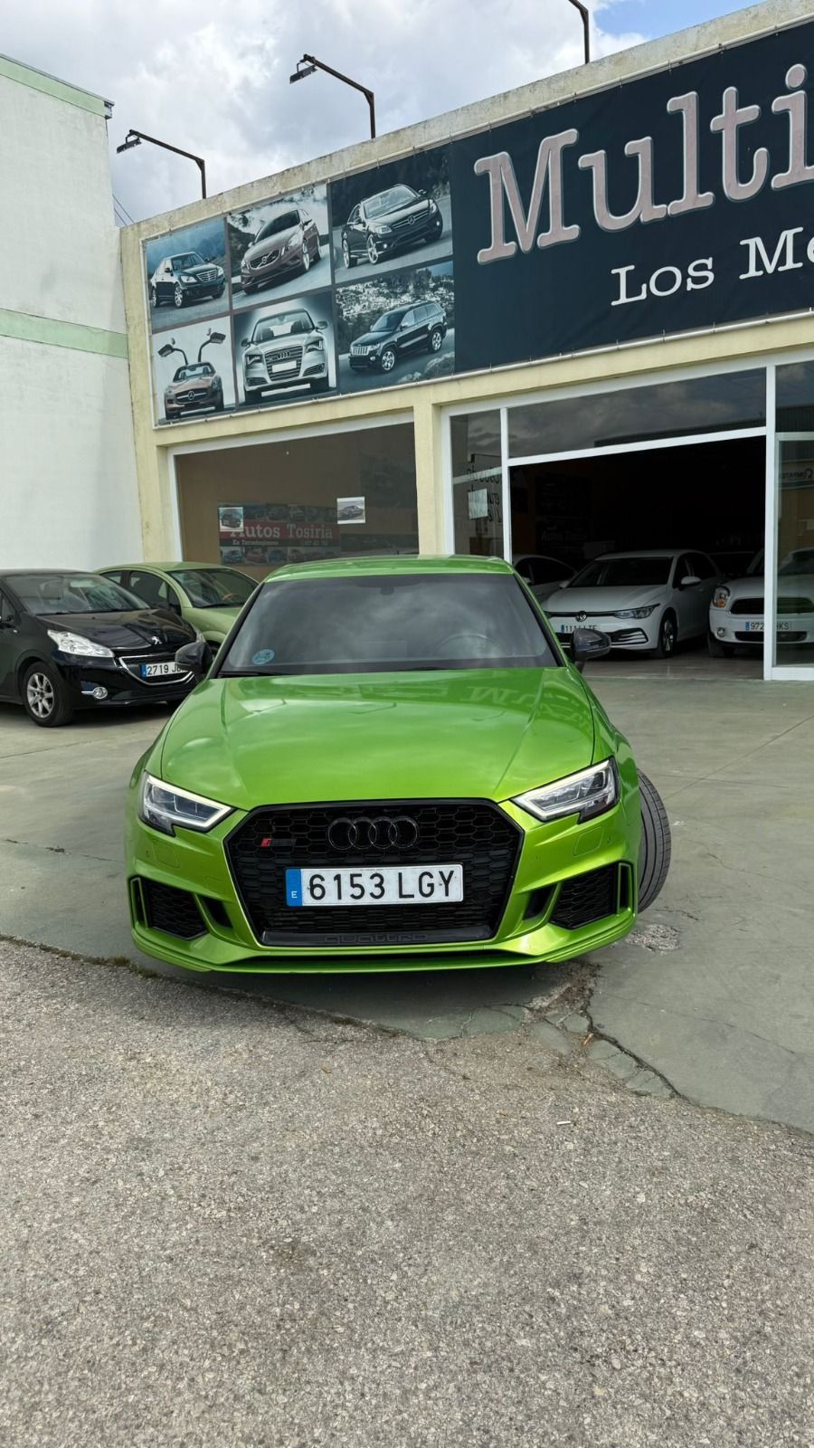 Un deportivo de color verde brillante estacionado frente a un concesionario con boxes de garaje abiertos.