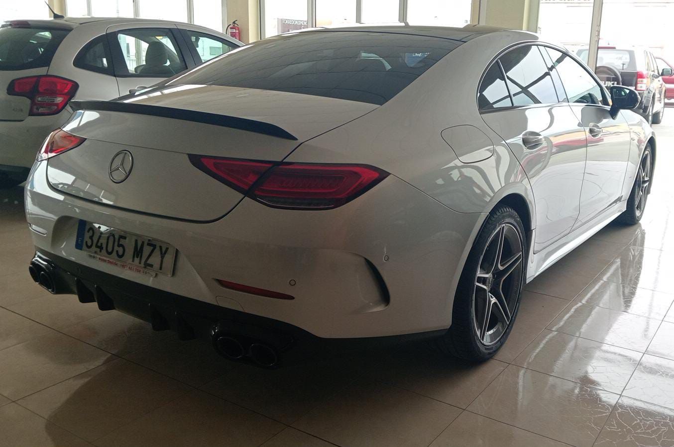 Sedán Mercedes plateado estacionado en el interior de una sala de exposición, vista trasera de tres cuartos.