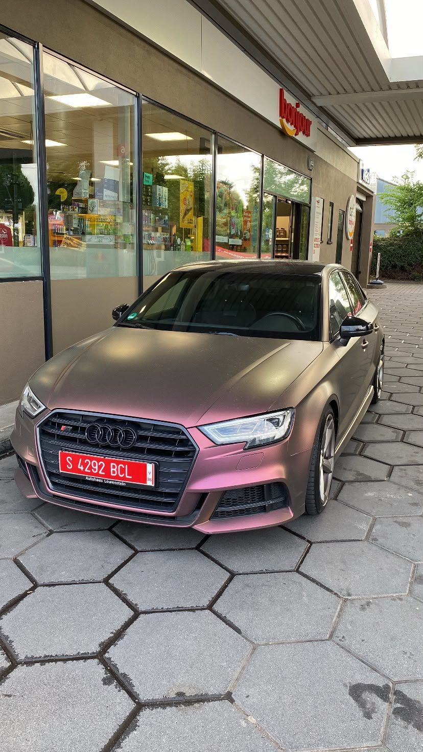 Un sedán rosa estacionado frente a una tienda con ventanas de cristal y una pasarela cubierta.