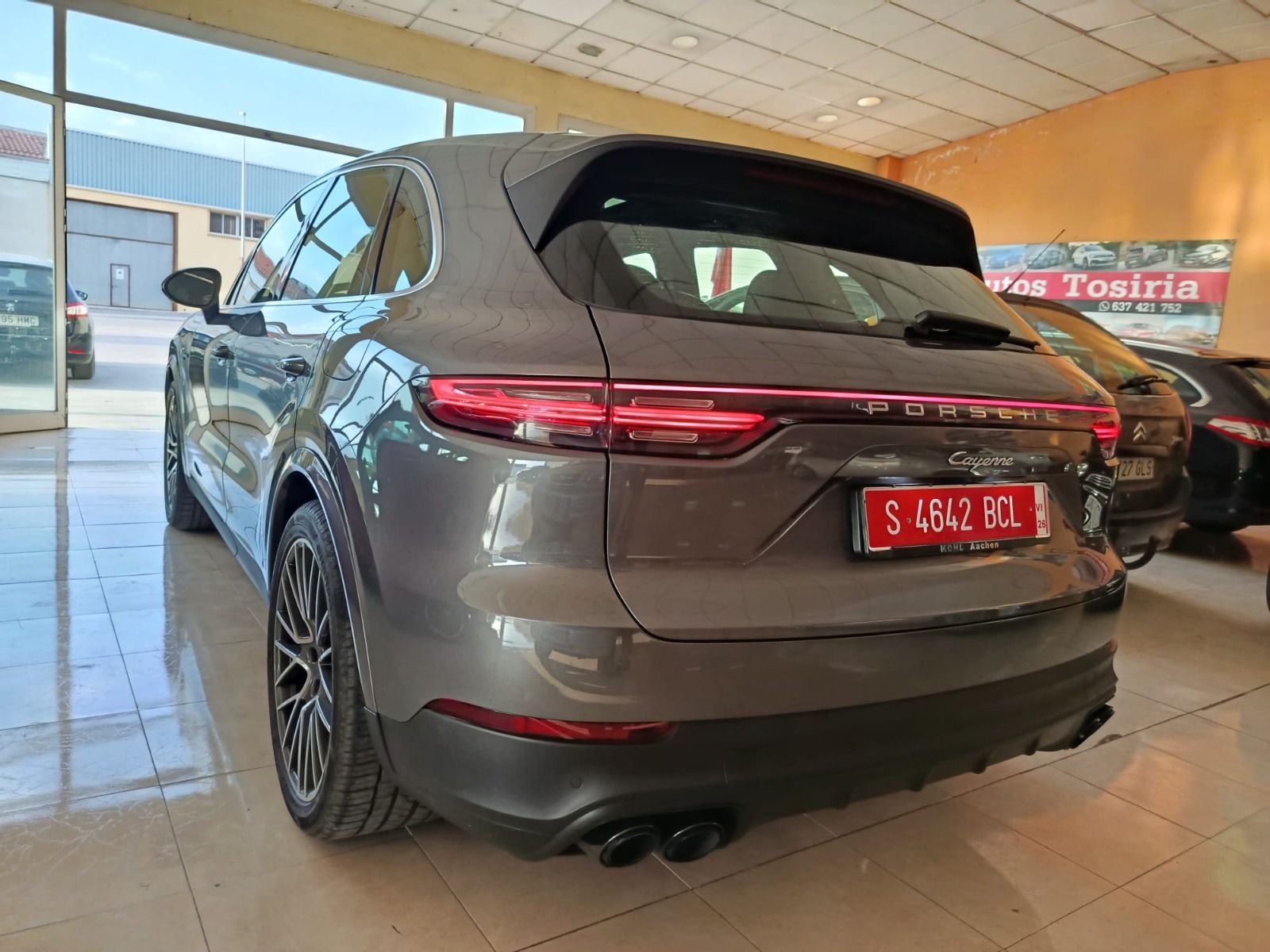 SUV gris en una sala de exposición, vista trasera con matrícula roja y luces traseras visibles.