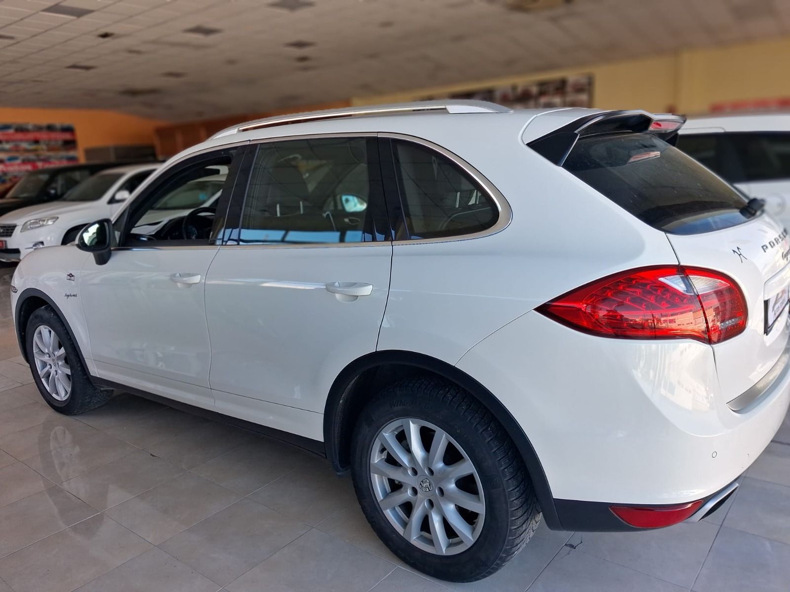 SUV blanco estacionado en el interior de una sala de exposición, vista trasera de tres cuartos.