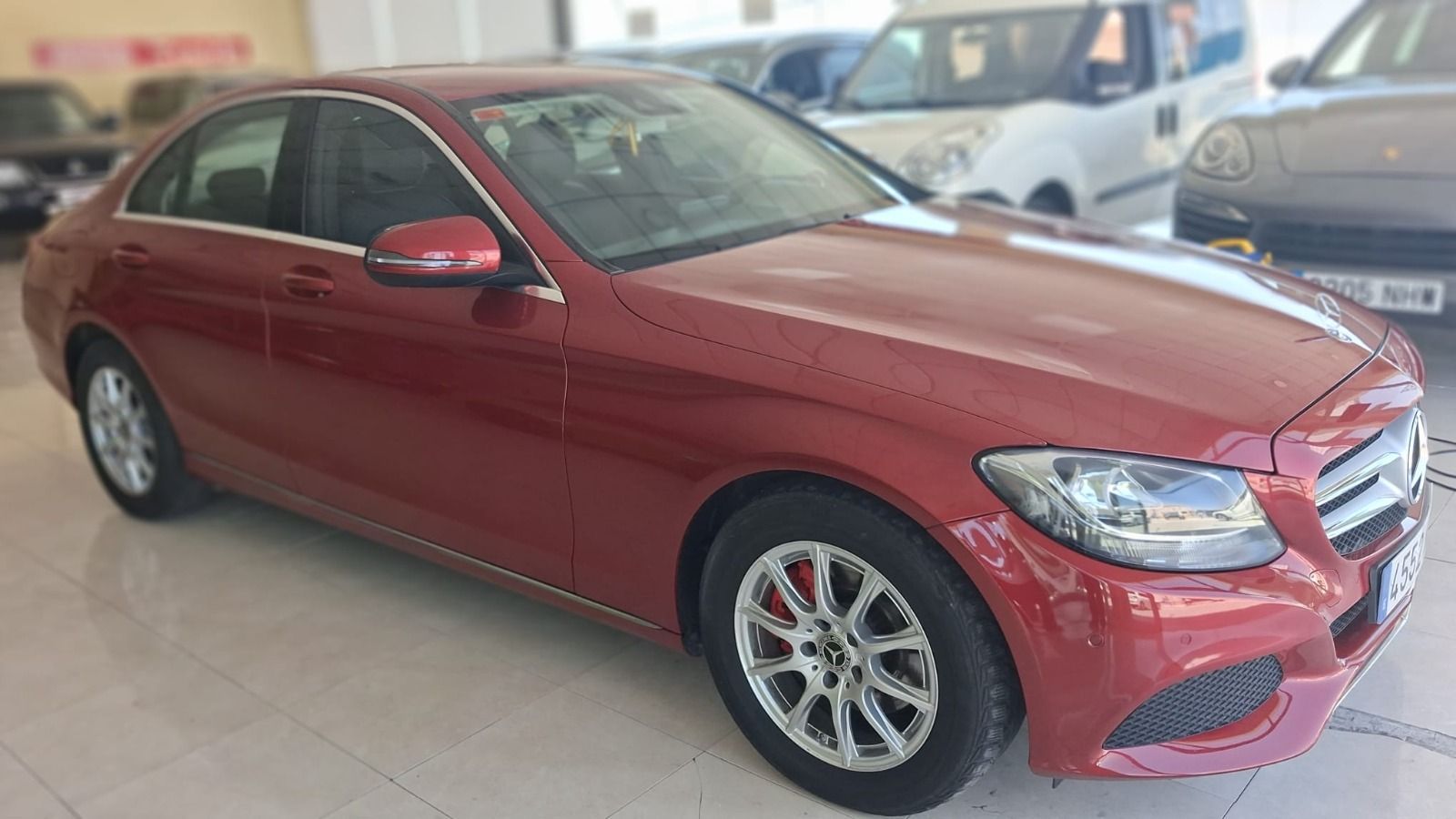Un sedán Mercedes rojo estacionado en el interior de una sala de exposición.