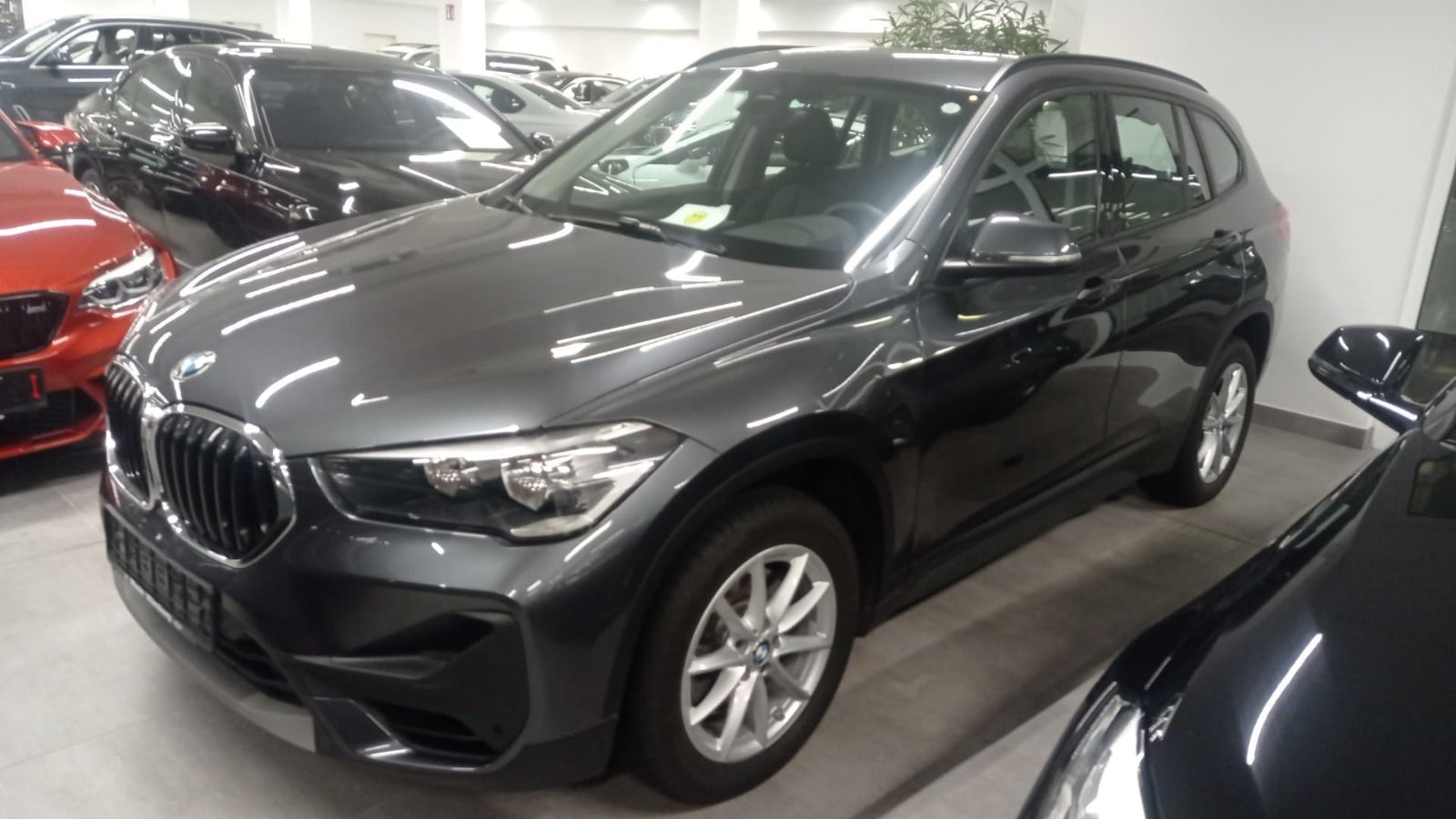 SUV BMW de color gris oscuro en una sala de exposición, visto desde el lado frontal izquierdo.