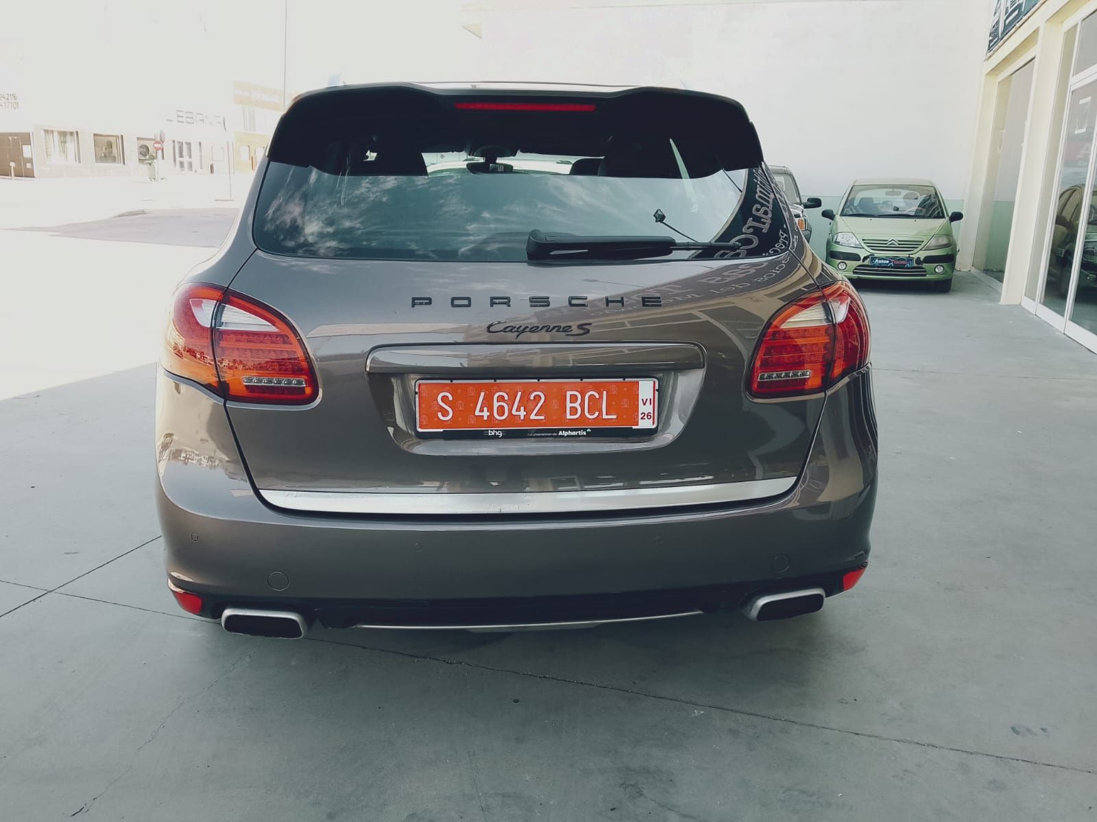 Vista trasera de un Porsche Cayenne marrón estacionado en un garaje, con matrícula naranja.