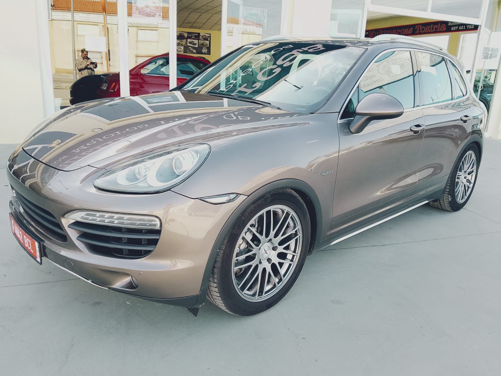 SUV Porsche gris estacionado al aire libre en una calle luminosa, vista frontal izquierda.