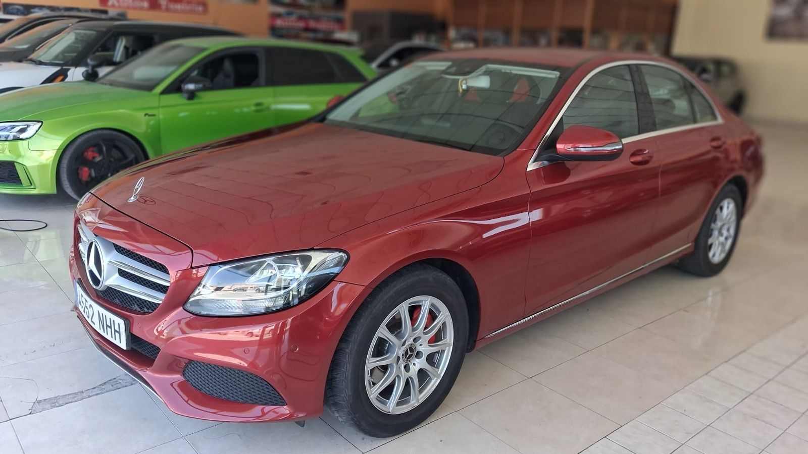 Un sedán Mercedes rojo estacionado en el interior, con un coche deportivo verde brillante al fondo.