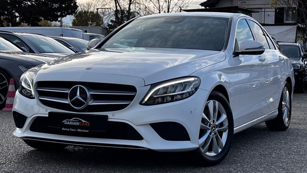 Mercedes sedán blanco estacionado al aire libre en el lote de un concesionario, vista frontal.
