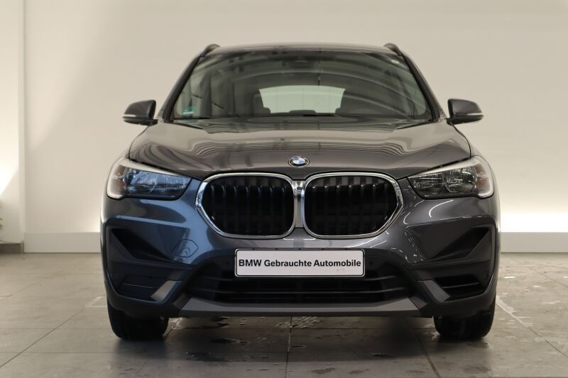 Vista frontal de un SUV BMW gris oscuro estacionado en el interior contra una pared lisa.