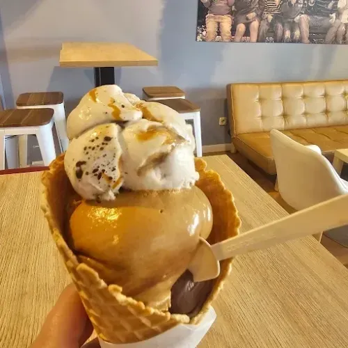 Cono de helado con sirope de caramelo sobre una mesa de café, con taburetes y un banco capitoné al fondo.