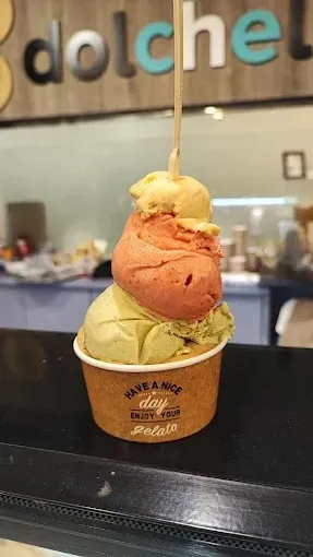Tres bolas de helado en un vaso con una cuchara de madera, expuestas en un mostrador.