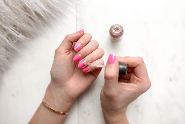 Una mujer se pinta las uñas con esmalte de uñas rosa.