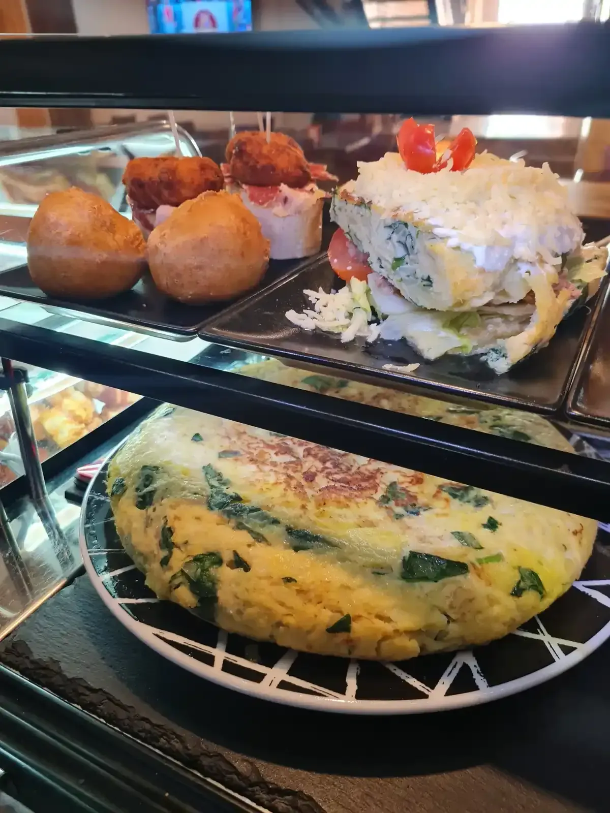 Vitrina con varias tapas españolas: tortilla de patatas, bolas fritas, bocadillo.